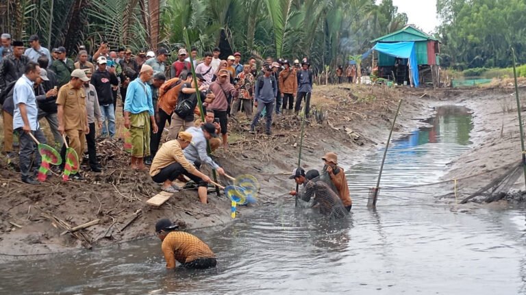 Sekelompok orang terlibat dalam kegiatan penangkapan ikan di tepi sungai dengan alat jaring.