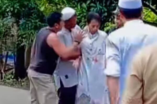 Sekelompok orang berdiri di jalan, dengan satu orang mengenakan pakaian putih dan dua orang lainnya berinteraksi di sekitarnya.