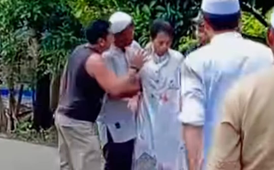 Sekelompok orang berdiri di jalan, dengan satu orang mengenakan pakaian putih dan dua orang lainnya berinteraksi di sekitarnya.