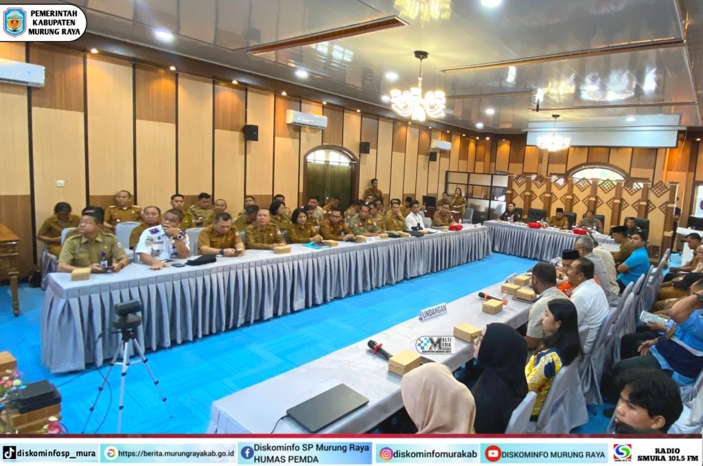 Heriyus Bupati Murung Raya menghadiri Musrenbang RKPD 2027 bersama Wabup Rahmanto Muhidin dalam ruang rapat berpanel kayu coklat, karpet biru, dan barisan peserta beruniform coklat