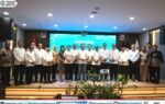 Suasana Rakernas APKASI XVII dengan Heriyus, Sarman Simanjorang, dan Delis Julkarson Hehi berdiri di depan panggung, berlatar layar biru.