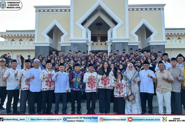 Rombongan 73 jamaah calon haji bersama Heriyus dan Pirman Prihatin berpose di depan Masjid Agung Puruk Cahu, mengenakan batik dan topi haji.