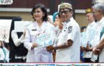 Heriyus menerima tiga penghargaan stunting Kalteng 2026 dengan sertifikat dari Linae Victoria Aden di aula, berpakaian putih dan kopiah bermotif.