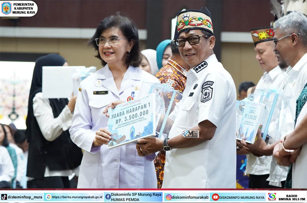 Heriyus menerima tiga penghargaan stunting Kalteng 2026 dengan sertifikat dari Linae Victoria Aden di aula, berpakaian putih dan kopiah bermotif.