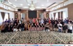 Kontingen Kabupaten Murung Raya untuk FBIM 2026 berfoto bersama di aula, dipantau Heriyus bersama Warnita Heriyus dan Jayadie Y. Dadi dengan karpet bermotif dan pakaian adat.