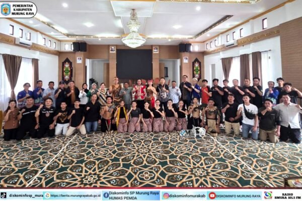 Kontingen Kabupaten Murung Raya untuk FBIM 2026 berfoto bersama di aula, dipantau Heriyus bersama Warnita Heriyus dan Jayadie Y. Dadi dengan karpet bermotif dan pakaian adat.