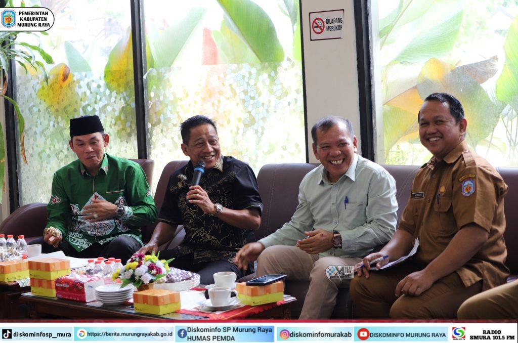 Suasana pertemuan Camat se-Kab. Murung Raya di Hotel Dandang Tingang, menampilkan Bupati Heriyus dan Rahmanto Muhidin dengan pakaian batik, tersenyum.