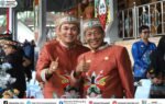 Heriyus dan Rahmanto Muhidin tersenyum sambil mengacungkan jempol, mengenakan busana adat merah saat menghadiri HUT ke-76 Barito Utara.