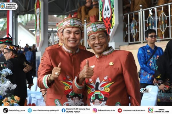 Heriyus dan Rahmanto Muhidin tersenyum sambil mengacungkan jempol, mengenakan busana adat merah saat menghadiri HUT ke-76 Barito Utara.