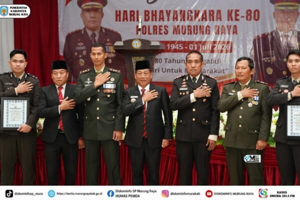 Para pejabat Murung Raya berdiri memberi hormat di depan banner Hari Bhayangkara ke-80 Polres Murung Raya pada acara syukuran di aula.