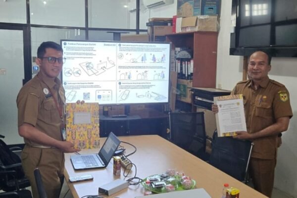Dua pejabat berseragam cokelat berdiri di ruang kantor sambil memegang berkas serah terima hibah perangkat Starlink.