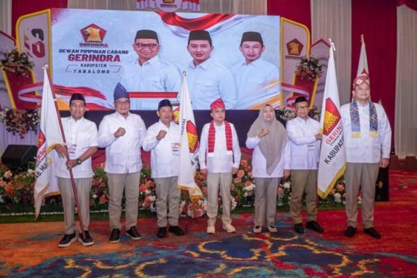 H. Noor Rifani berdiri bersama jajaran kader Gerindra Tabalong di depan panggung pengukuhan dengan bendera partai.