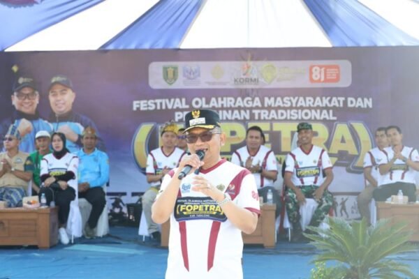 Seorang pembicara berjaket merah putih berbicara dengan mikrofon di depan panggung pembukaan FOPETRA 2026 di Tabalong.