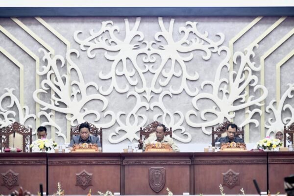 Edy Pratowo menghadiri rapat resmi di ruang sidang dengan panel kayu gelap dan ornamen ukiran putih di belakangnya