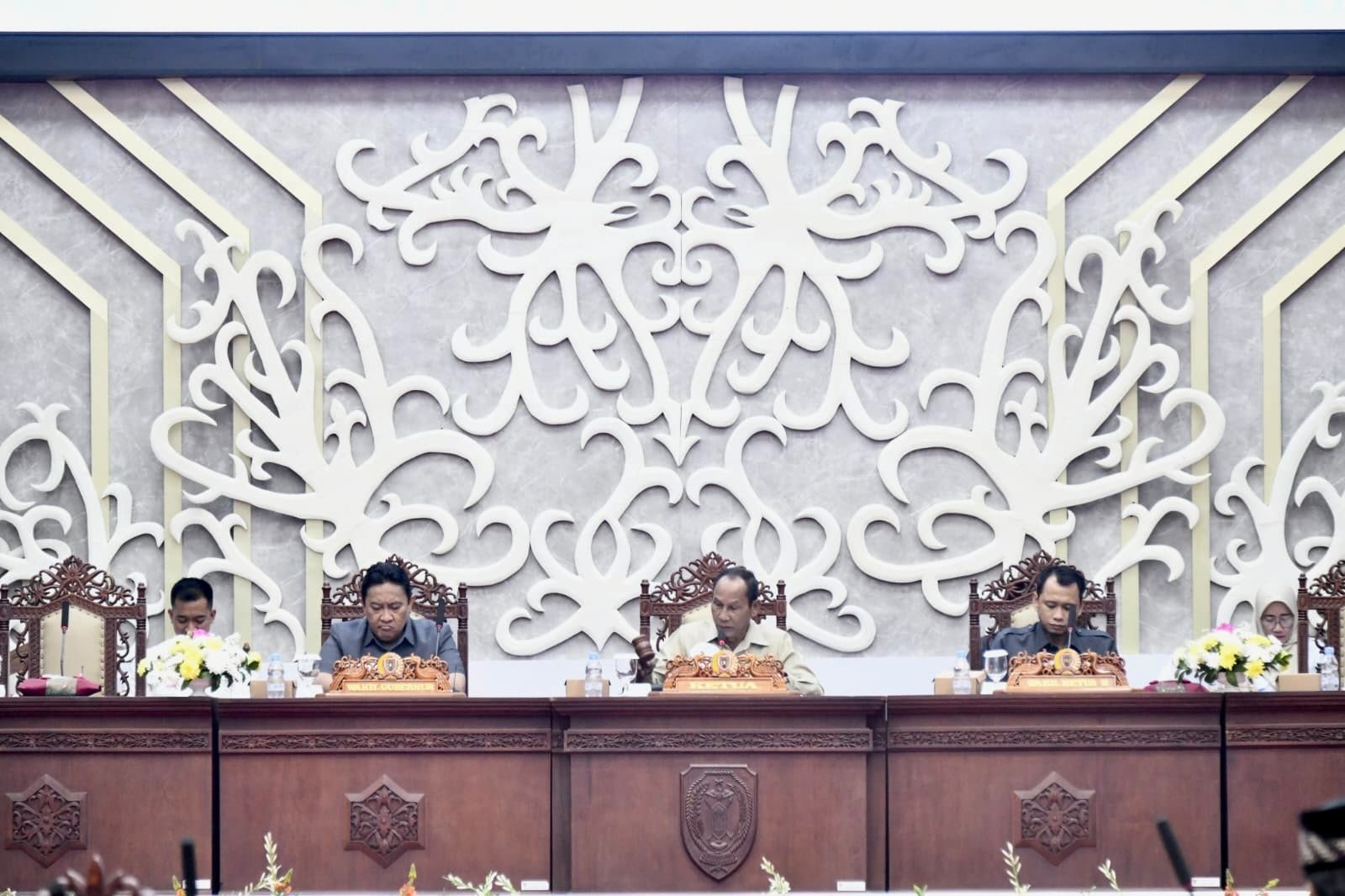 Edy Pratowo menghadiri rapat resmi di ruang sidang dengan panel kayu gelap dan ornamen ukiran putih di belakangnya